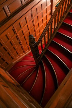 Beautifully designed curved staircase with red carpet and intricate woodwork, creating a classic and timeless appeal.