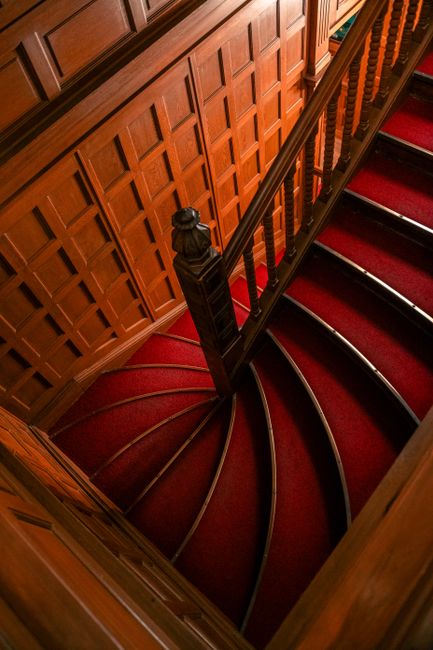 Beautifully designed curved staircase with red carpet and intricate woodwork, creating a classic and timeless appeal.