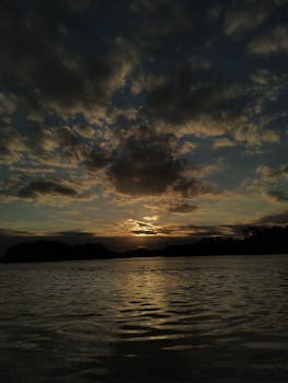 Serene sunset with dramatic clouds reflected on the lake surface, creating a tranquil and picturesque scene.