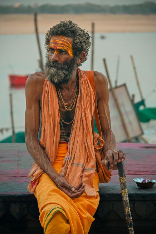 Free Traditional Indian Sadhu sitting beside the Ganges River in Varanasi, India, wearing saffron robes and face paint. Stock Photo