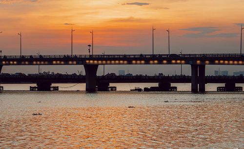 Free Serene view of a bridge at sunset with calm waters reflecting the vibrant sky. Stock Photo