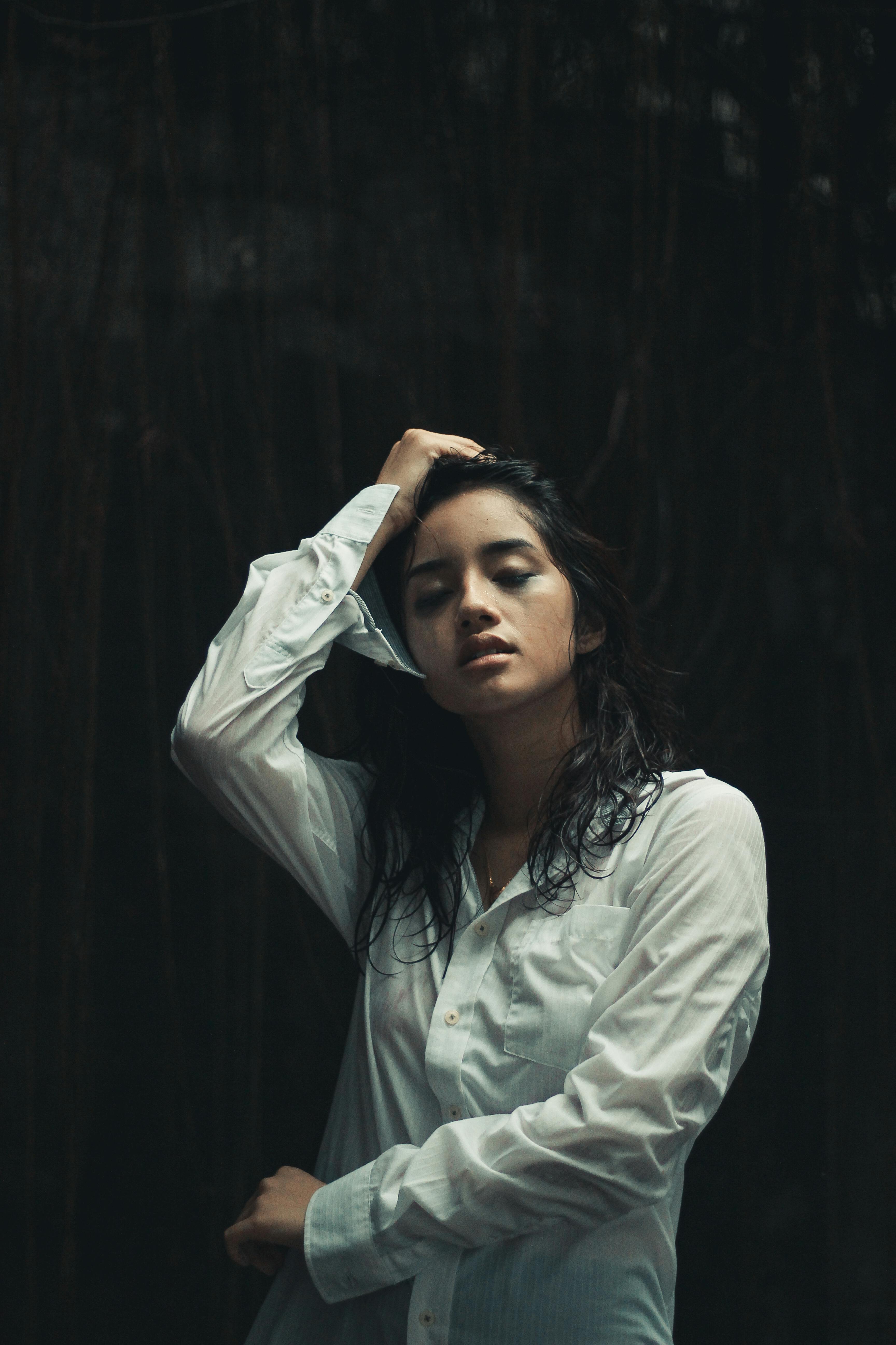 在黑暗背景下，一位闭着眼睛的女人摆出姿势，营造出戏剧性肖像画般的宁静氛围