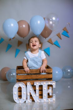 A joyful baby celebrating their first birthday with colorful balloons and a wooden crate.