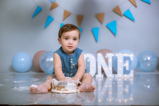 Cute baby enjoying a cake smash during a first birthday photo shoot with festive decorations.
