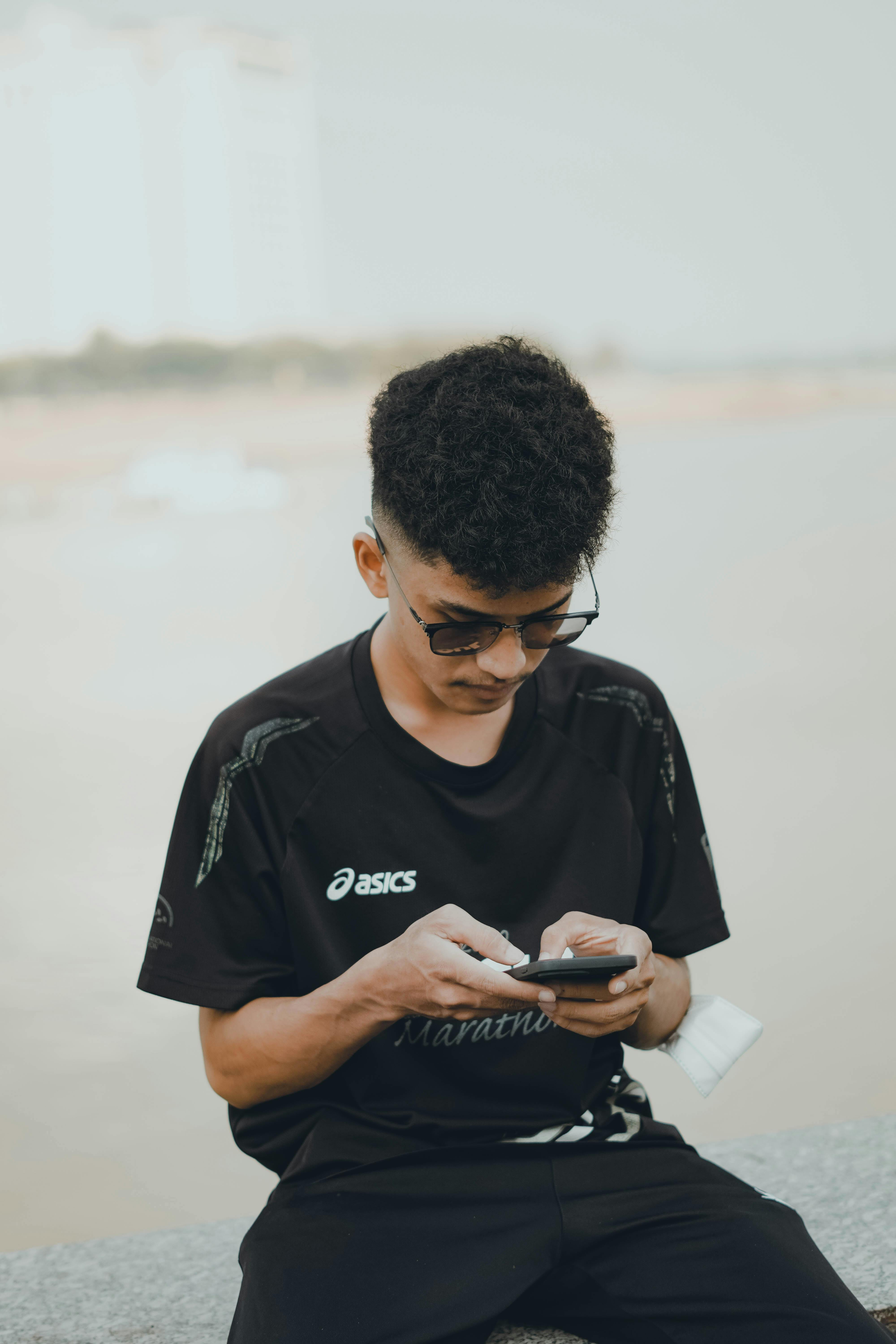 Gratuit Tânăr ocazional în ochelari de soare își verifică telefonul lângă un râu în aer liber. Fotografie de stoc