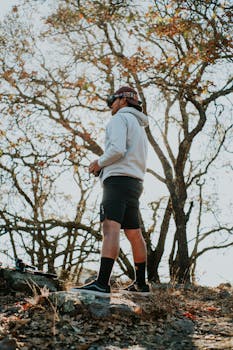 A man wearing VR goggles operates an FPV drone in a scenic outdoor woodland setting.