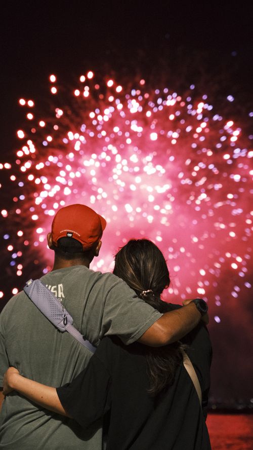 Free A couple embraces while watching a vibrant fireworks display at night. Stock Photo
