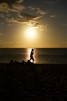 A person walks on the beach during a stunning sunset, creating a beautiful silhouette.