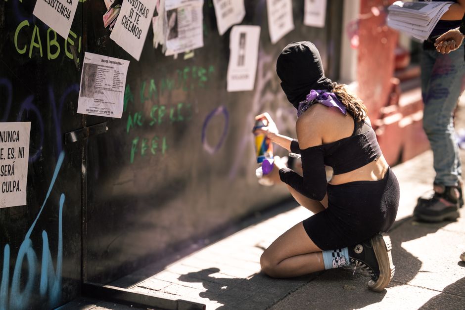 Protester spray-painting graffiti on wall during women's rights demonstration in Mexico City.