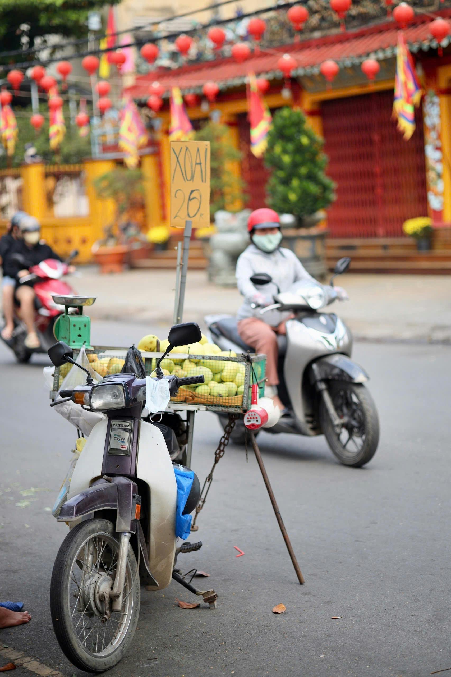 Street vendor on scooter selling mangoes with price sign in vibrant market setting.