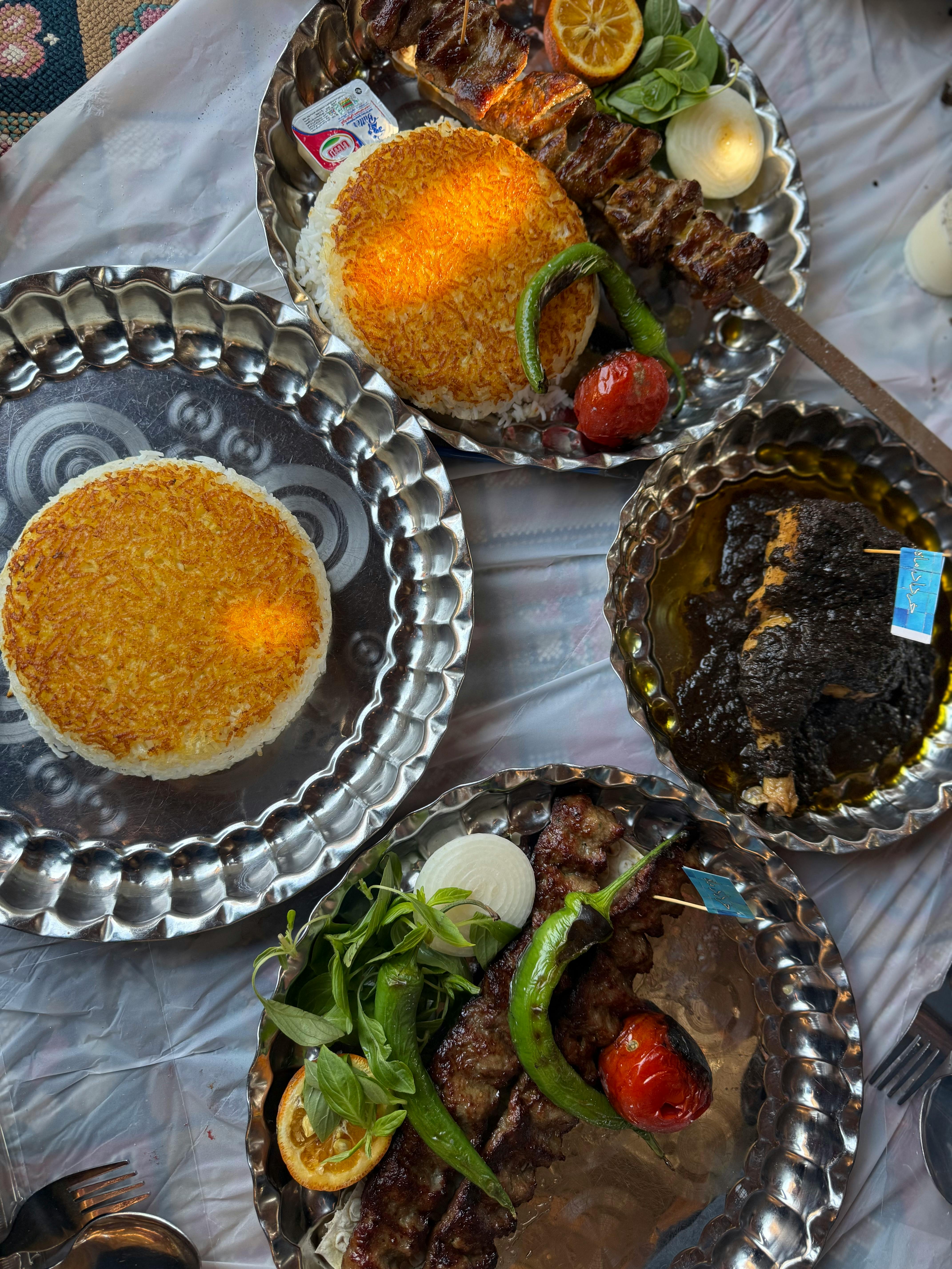 Plates of delicious grilled kebabs with saffron rice and greens on a table.