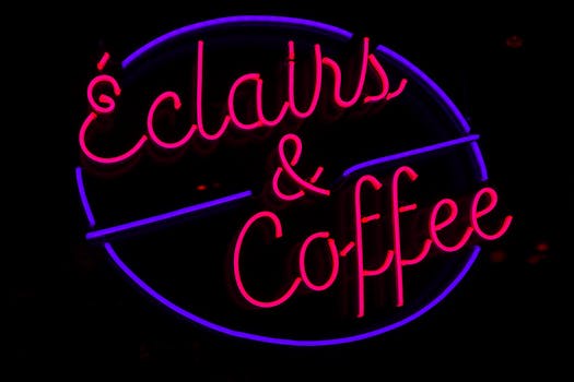 Bright neon sign reads 'Éclairs & Coffee', adding a retro vibe to city nights.