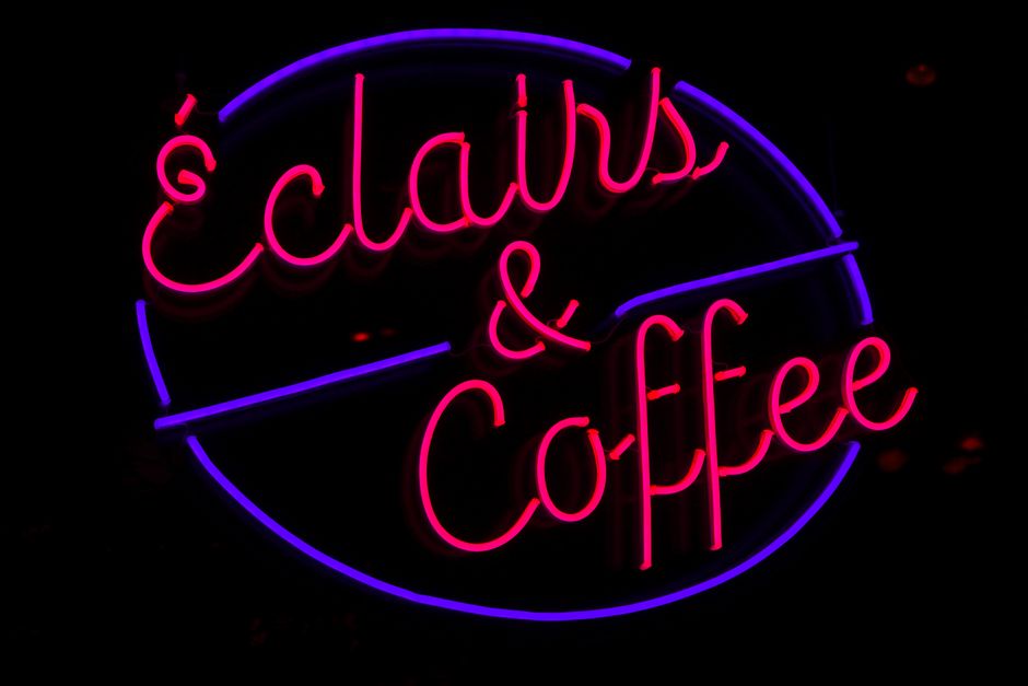 Bright neon sign reads 'Éclairs & Coffee', adding a retro vibe to city nights.