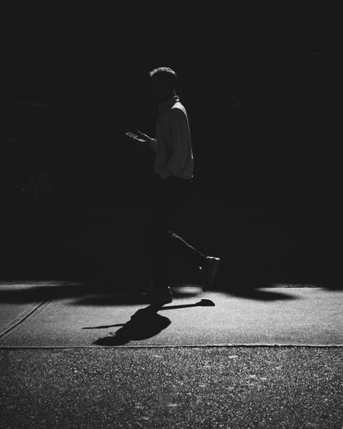 Free Silhouette of a person walking across a dimly lit street at night, creating a moody urban scene. Stock Photo