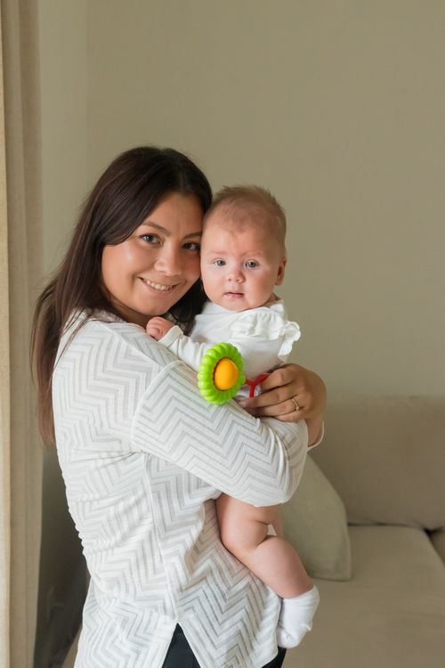 Free A loving mother holding her baby with a toy flower, creating a warm family moment. Stock Photo