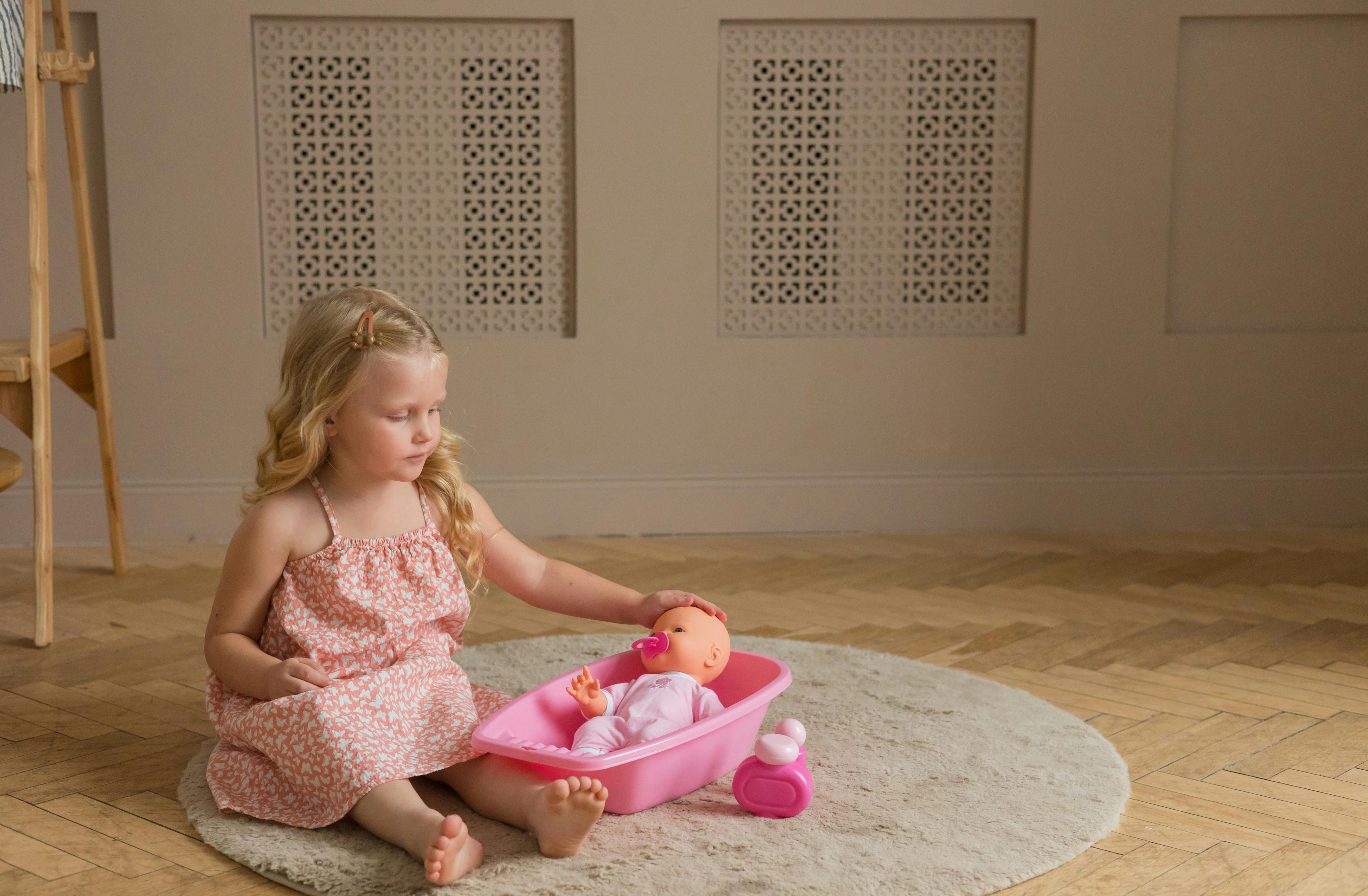 Young girl playing with a doll in a tub, enjoying a quiet moment indoors.