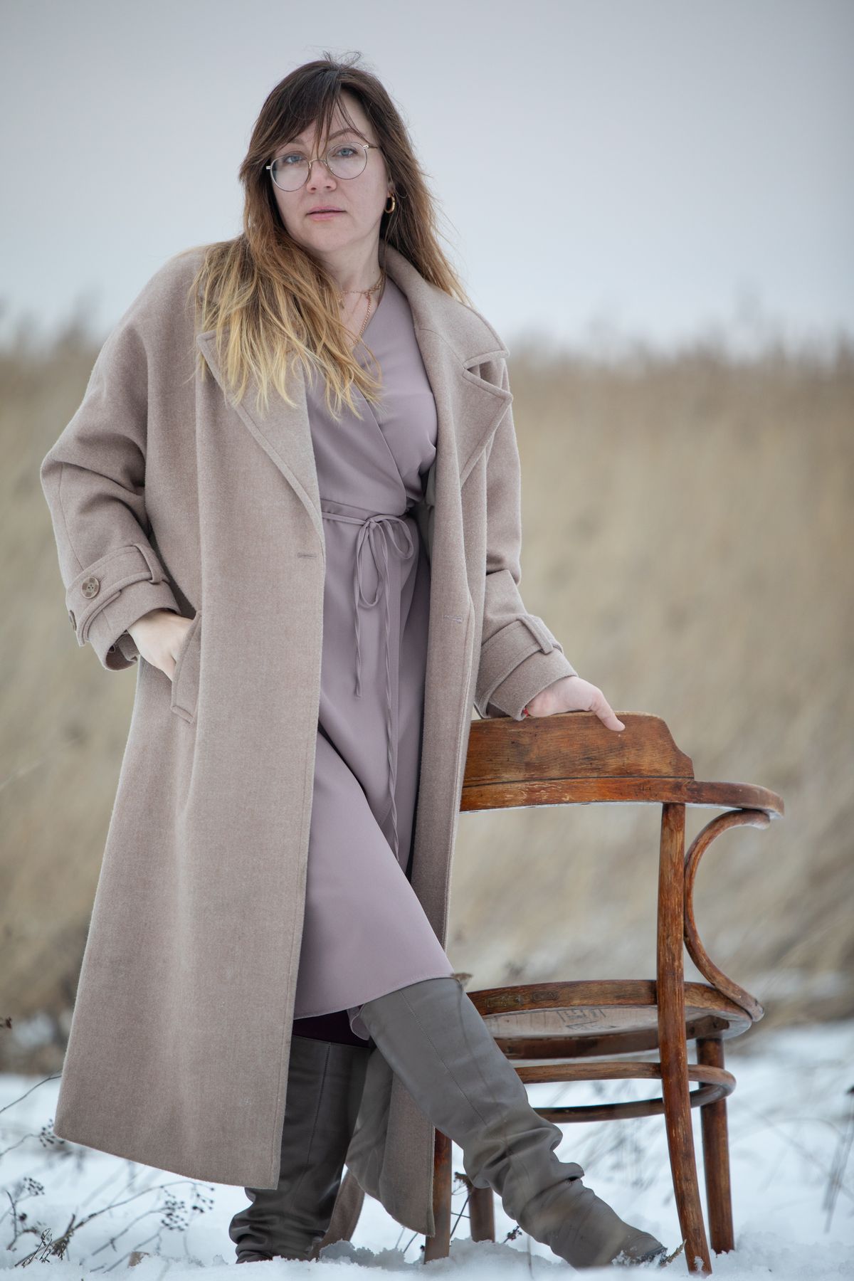 Woman wearing a long oversized beige wool coat with notched lapels, posed in a snowy field