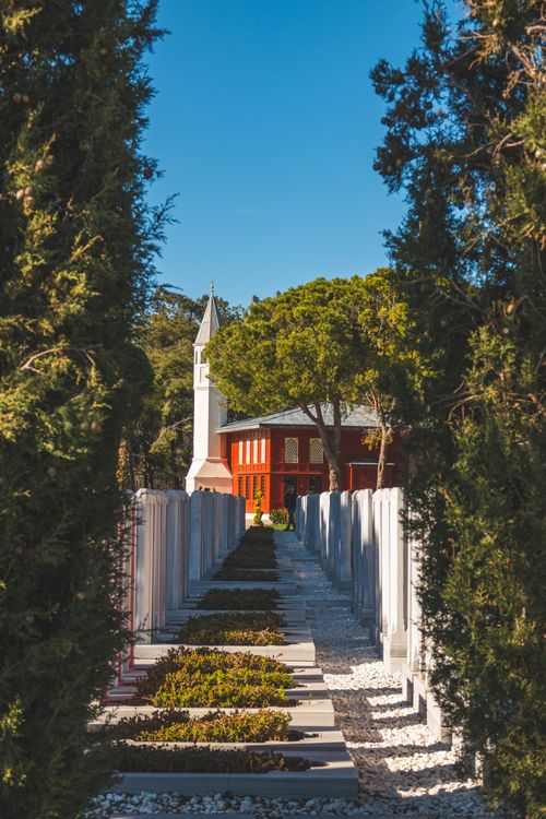 Free Peaceful cemetery pathway leads to a church under a clear blue sky, surrounded by nature. Stock Photo