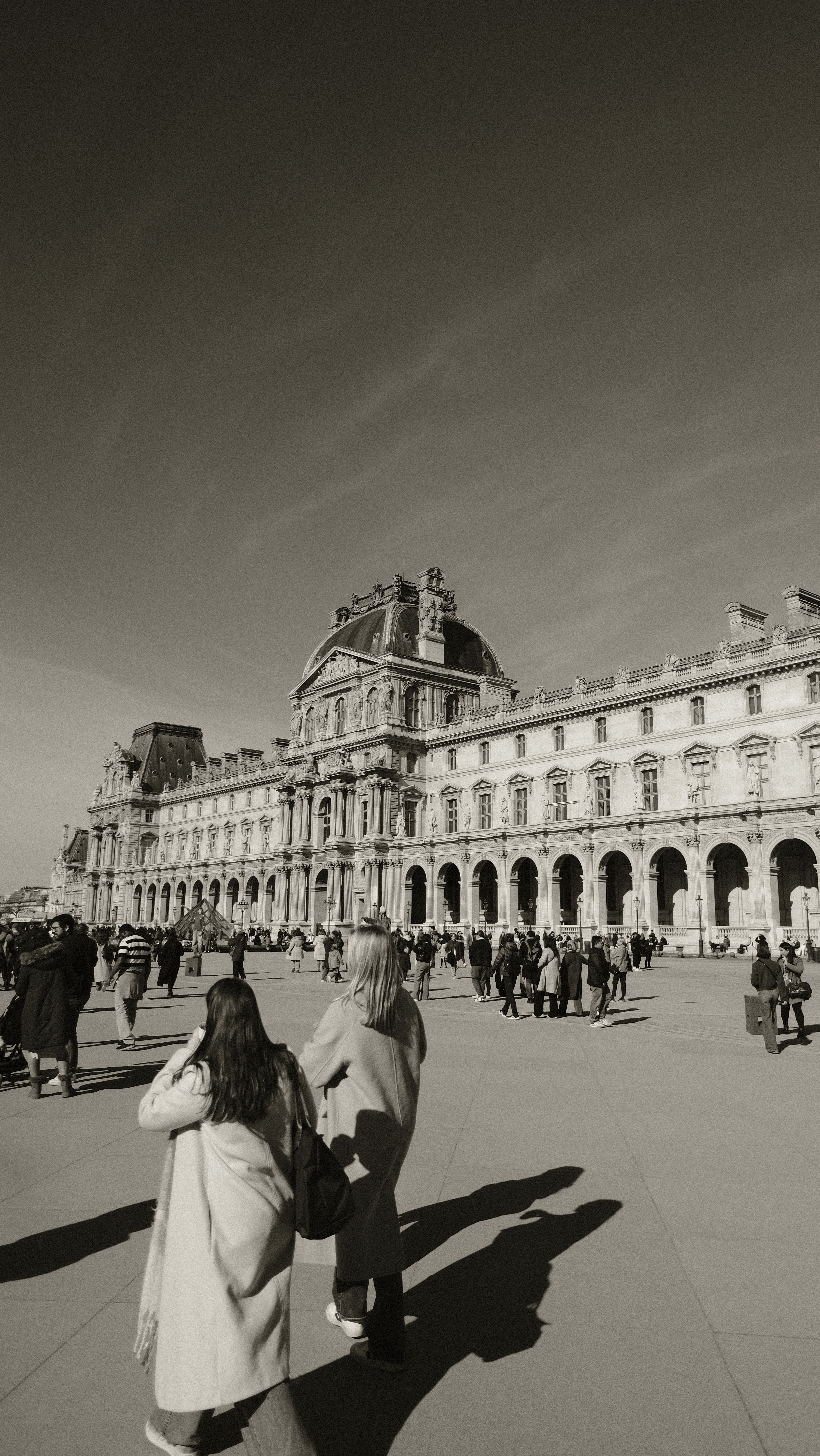 Crowded scene outside the Louvre Museum on a sunny day.