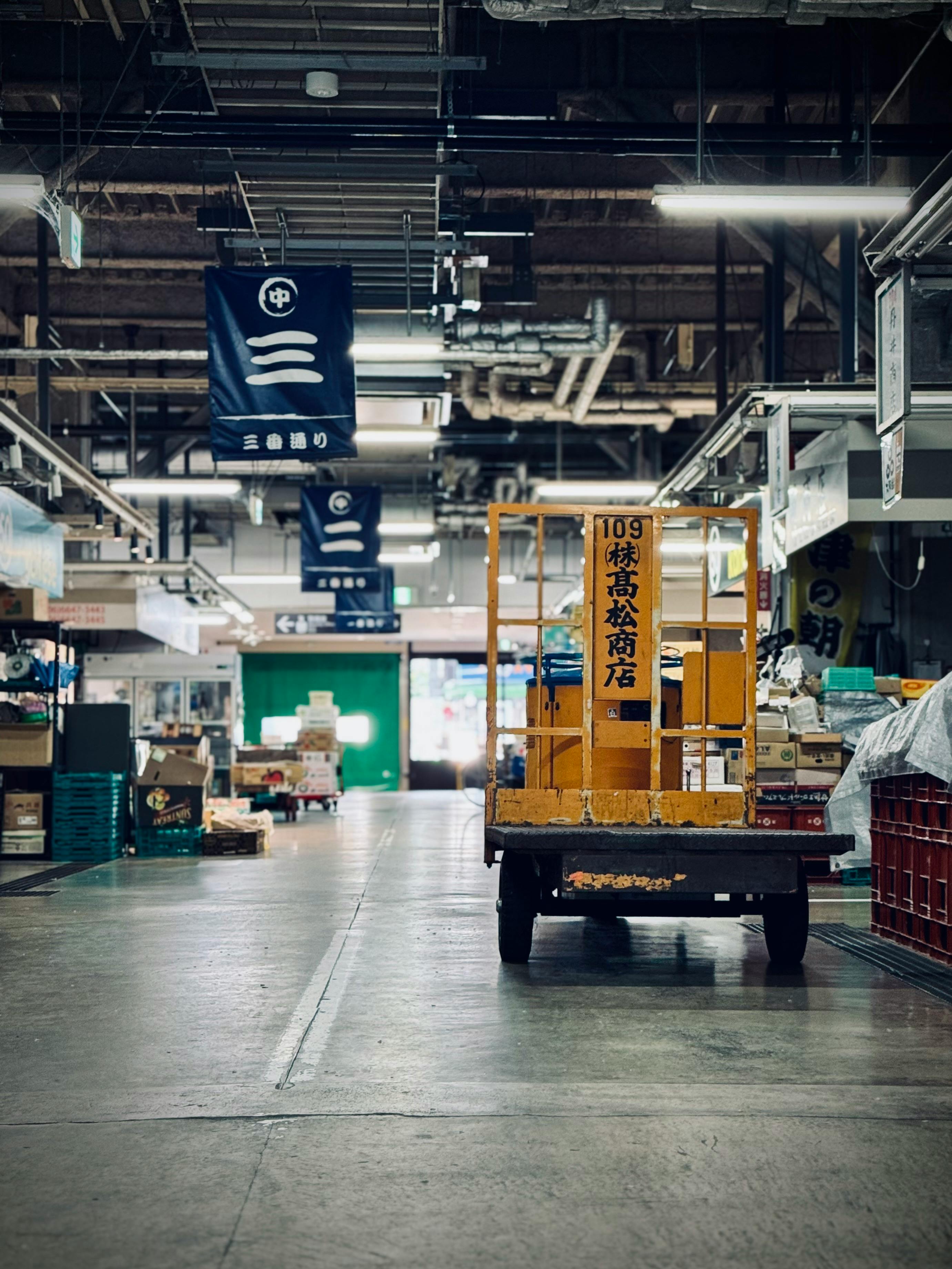 A quiet scene inside a Japanese market arcade featuring a yellow cart and overhead signage.