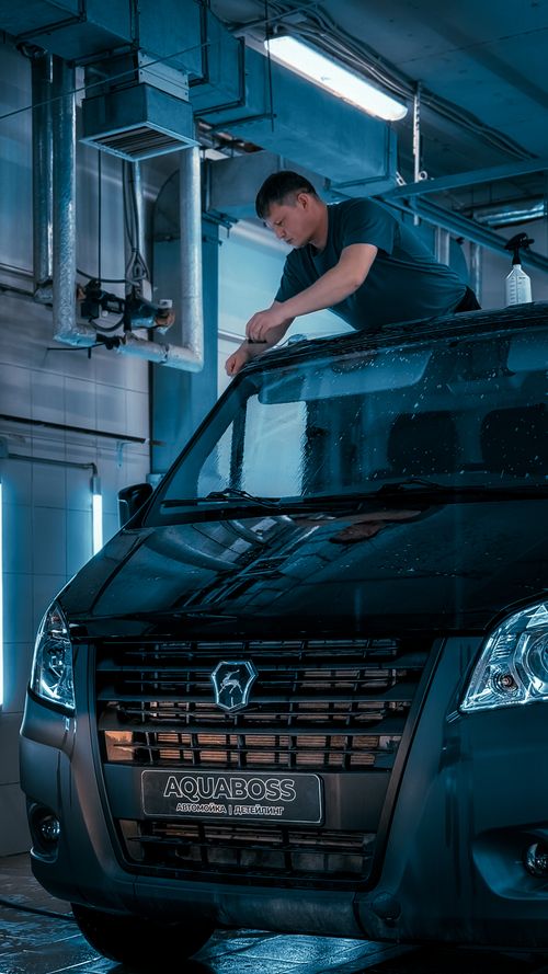 Free A man cleaning a black van in an indoor car wash, highlighting automotive service. Stock Photo