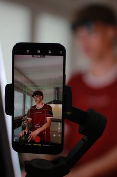 A filmmaker records himself in a kitchen using a smartphone and gimbal for content creation.