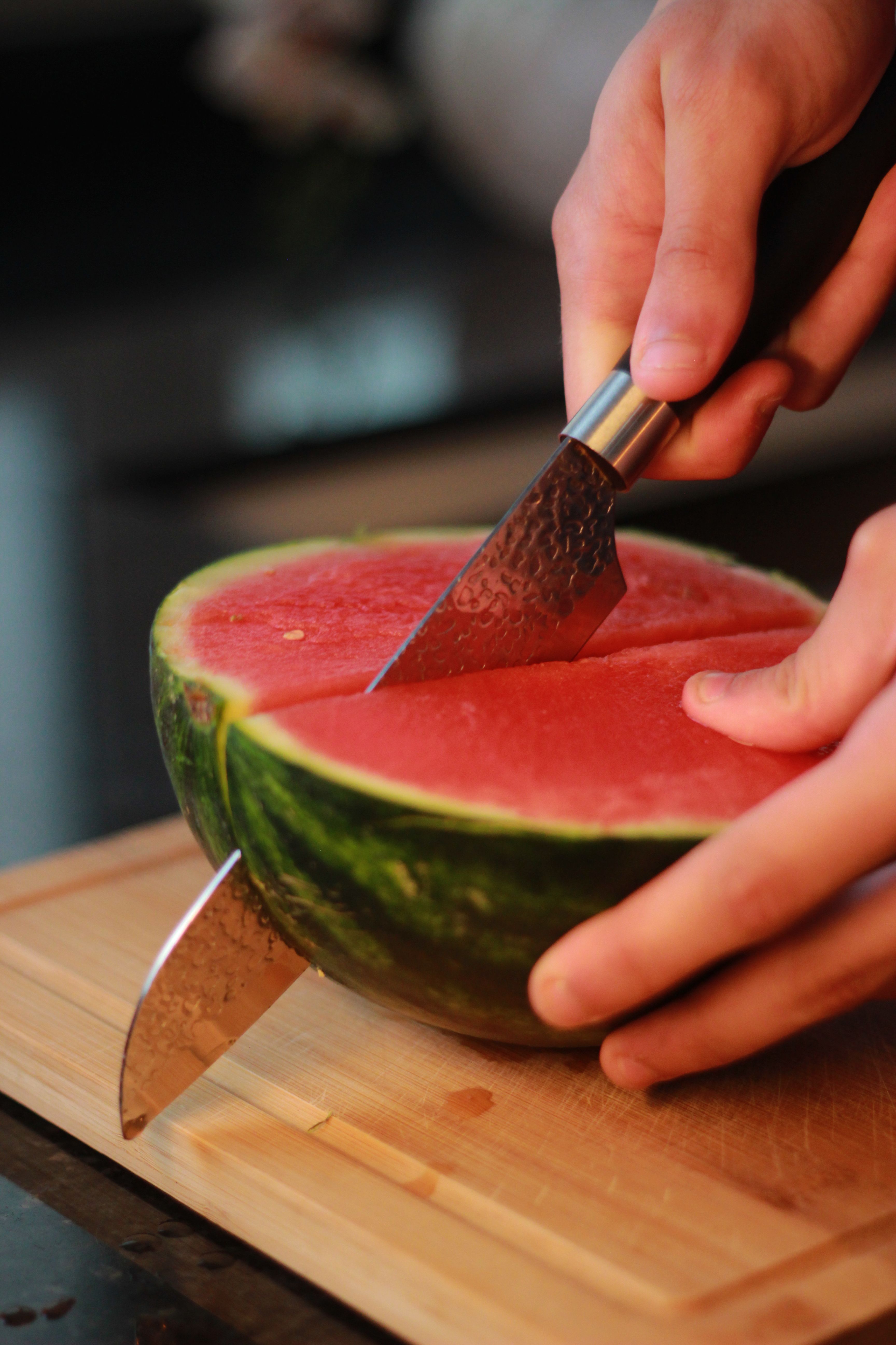 Hands slicing a ripe watermelon on a wooden board, showcasing fresh summertime preparation.