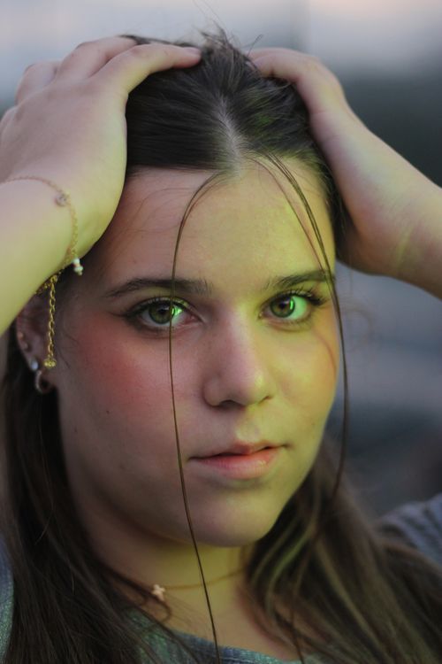 Free Close-up portrait of a young woman with intense gaze, hands on head. Stock Photo