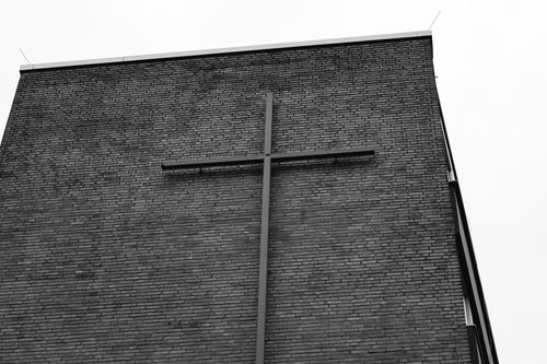 Free Black and white image of a church facade featuring a large cross against a brick wall in Düsseldorf, Germany. Stock Photo