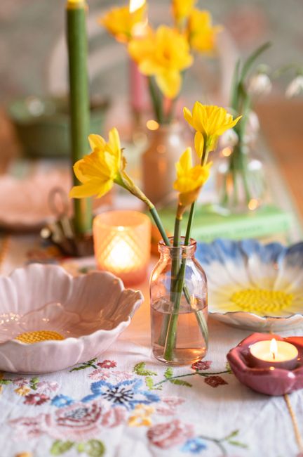 Charming spring table setup featuring daffodils, candles, and embroidered cloth.