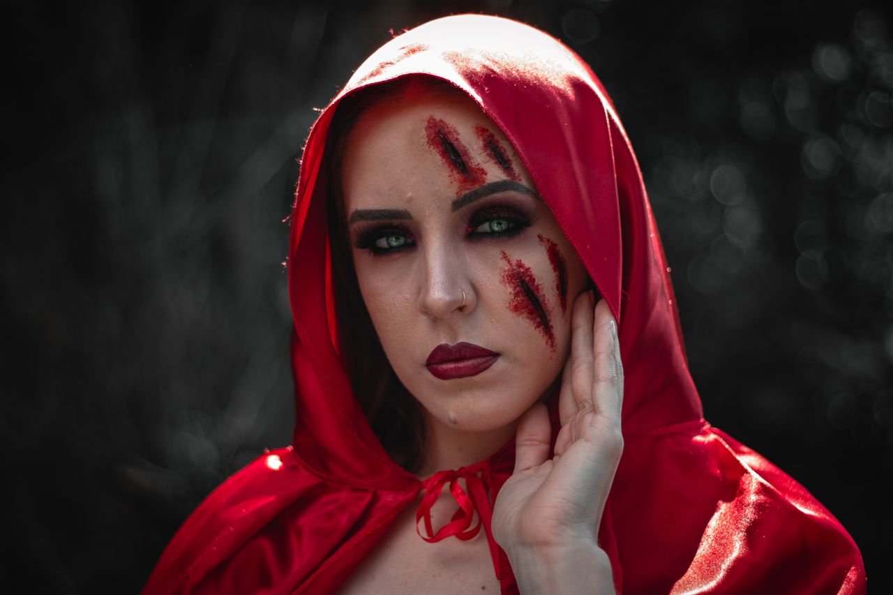 a haunting portrait of a woman in a red hood with dramatic makeup and
