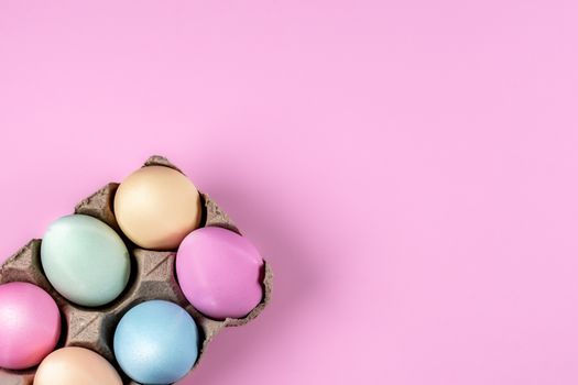 Pastel-colored Easter eggs in a carton on a pink background, perfect for spring themes.