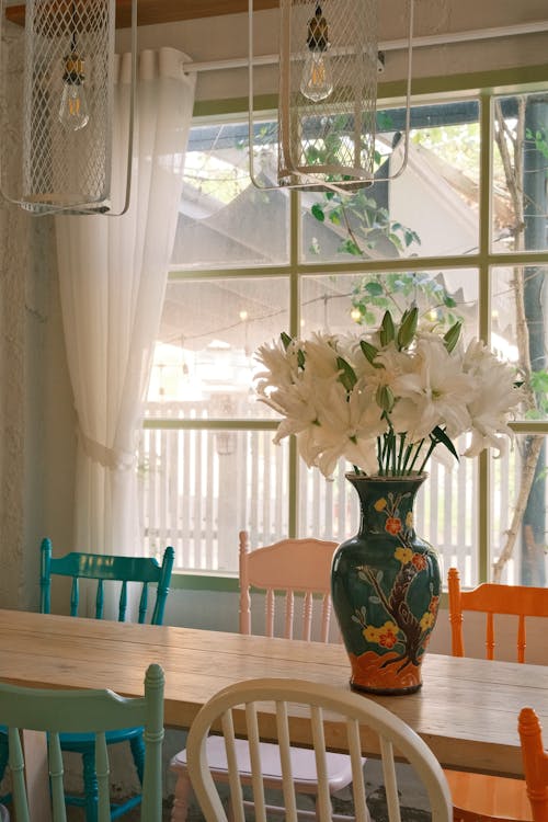 Free Bright dining area featuring a floral vase centerpiece with colorful vintage chairs. Stock Photo