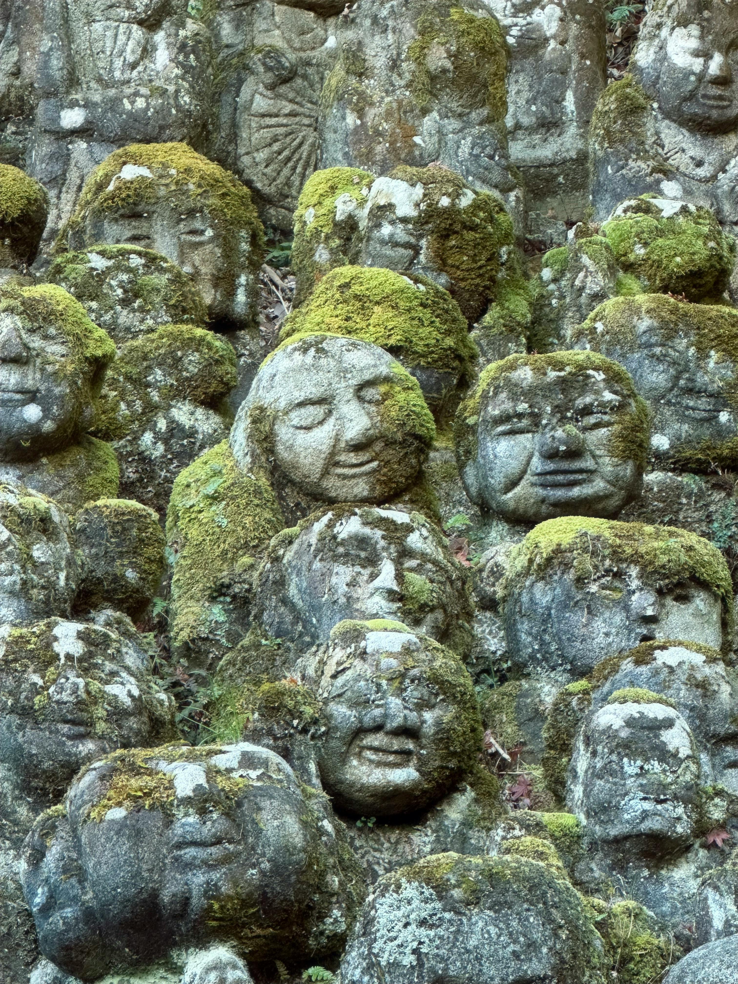Weathered stone statues of arhats covered with moss in a serene Japanese garden.