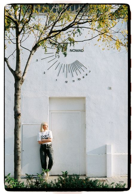 A person leans against a white wall with a modern sundial and 'NOMAD' written above.