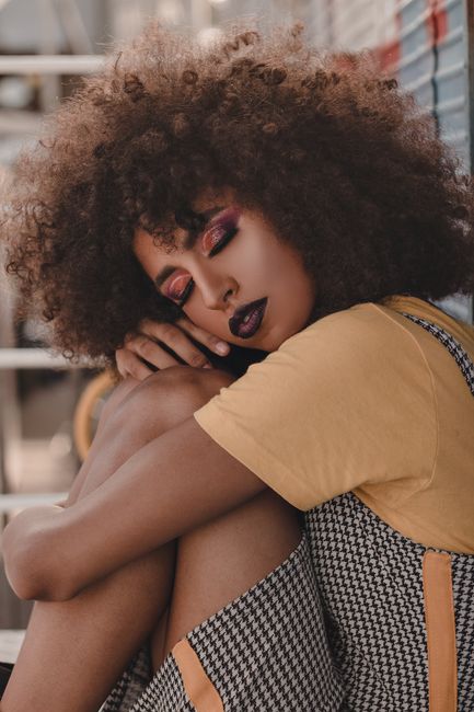 Elegant outdoor portrait of a woman with afro hair in fashionable attire, exuding style and glamour.