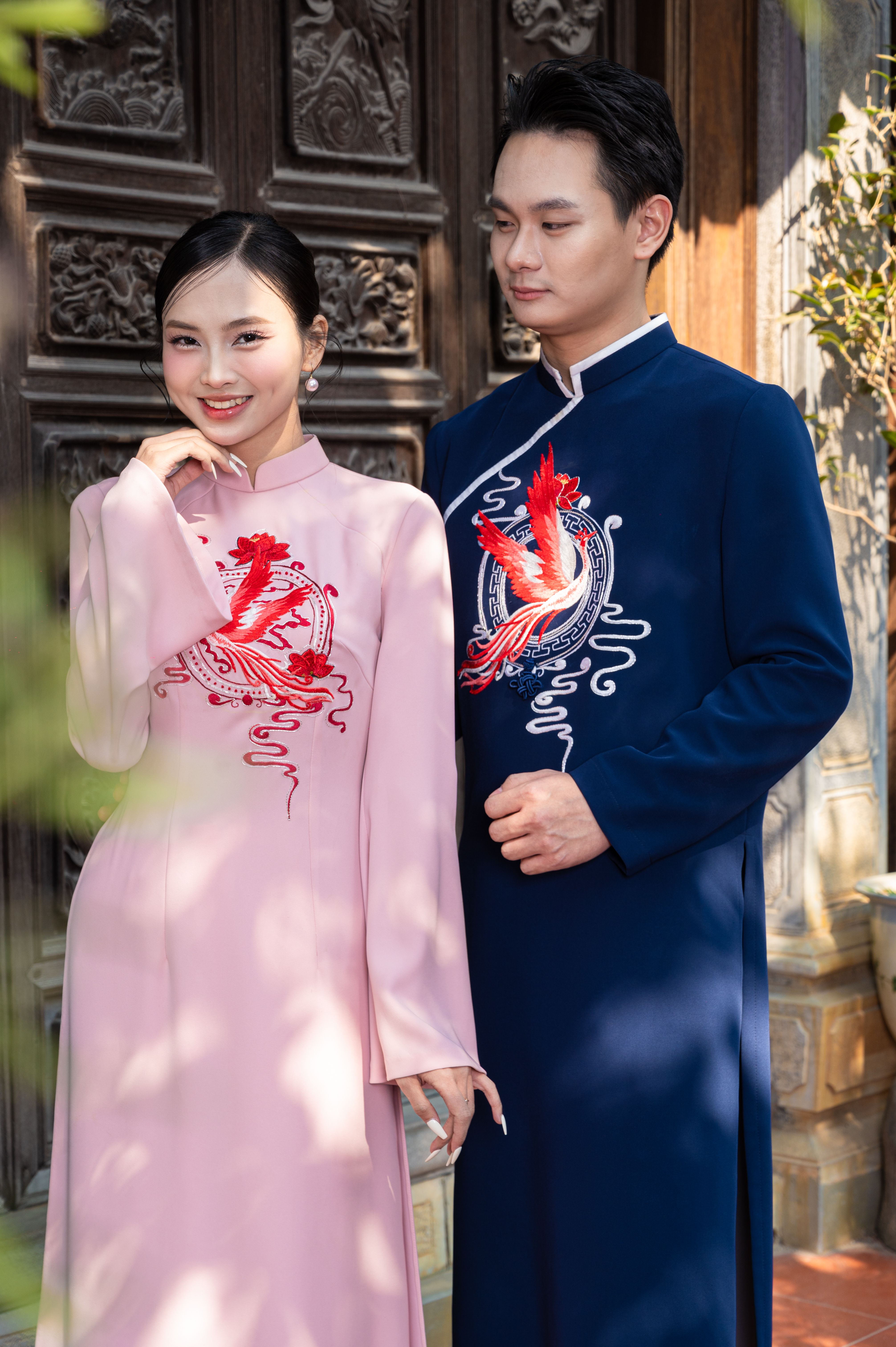 A joyful couple dressed in traditional Asian clothing poses outdoors.
