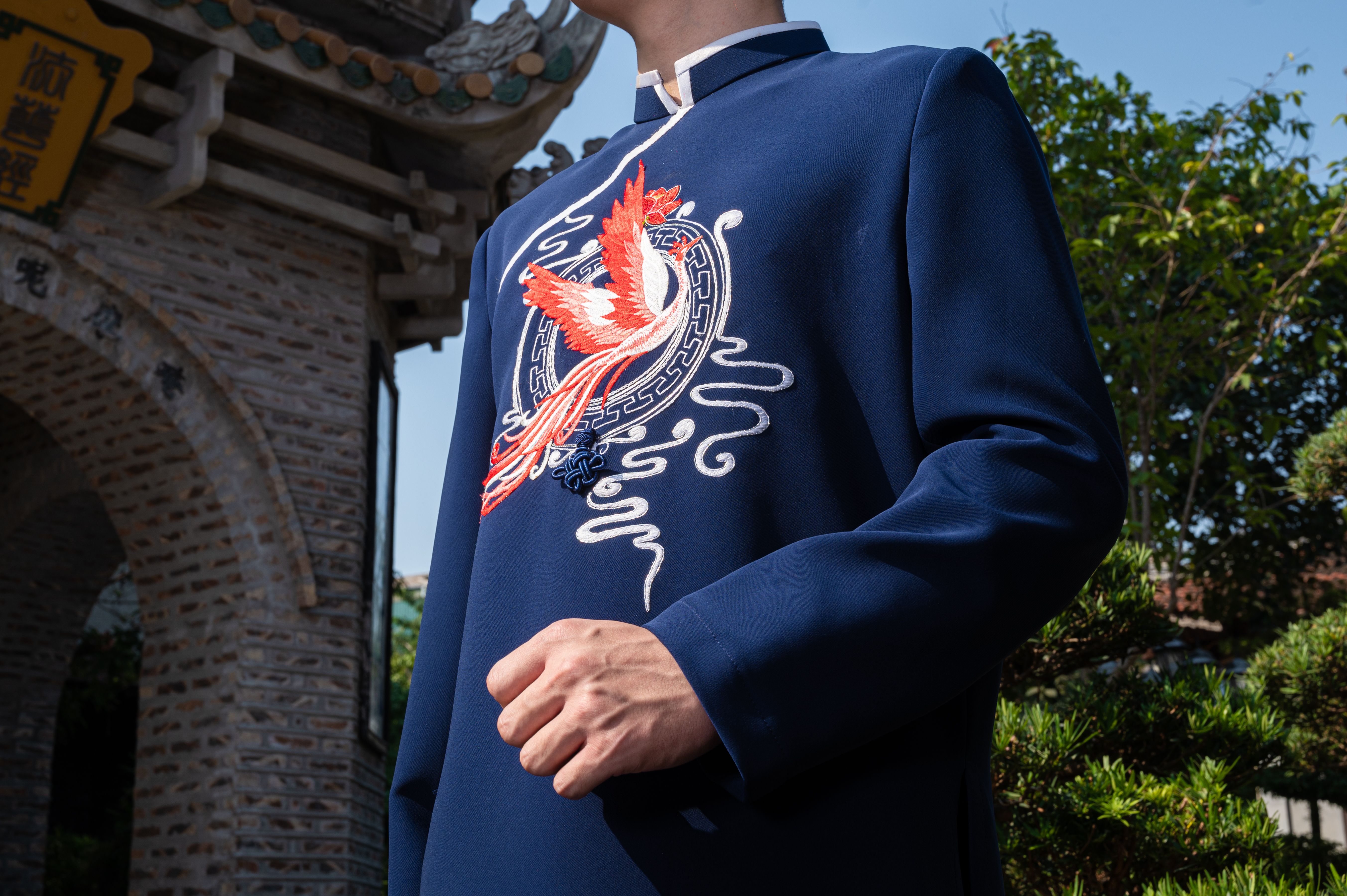 Close-up of a man wearing a traditional Chinese jacket with bird embroidery outdoors in sunny setting.