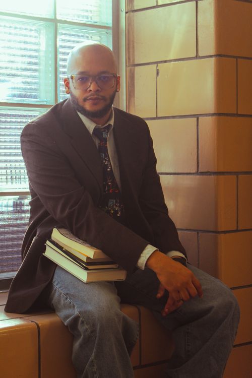 Free Thoughtful man seated with books near a window. Stock Photo