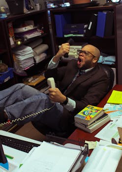 A stressed man in an office angrily shouts into a phone amidst cluttered desk.