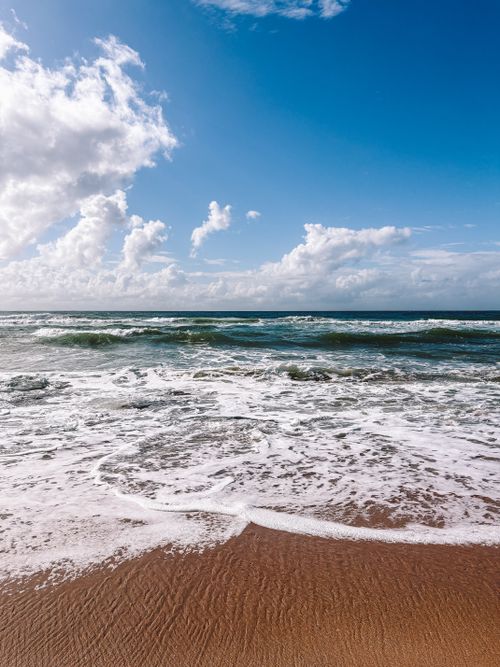Free Tranquil beach scene with gentle waves and blue sky, perfect for relaxation themes. Stock Photo