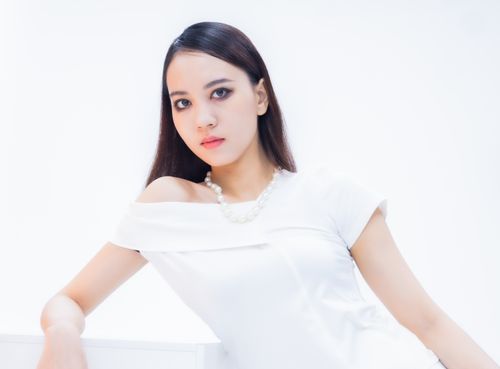 Free Stunning portrait of a woman in a white dress with a pearl necklace, set against a bright background. Stock Photo