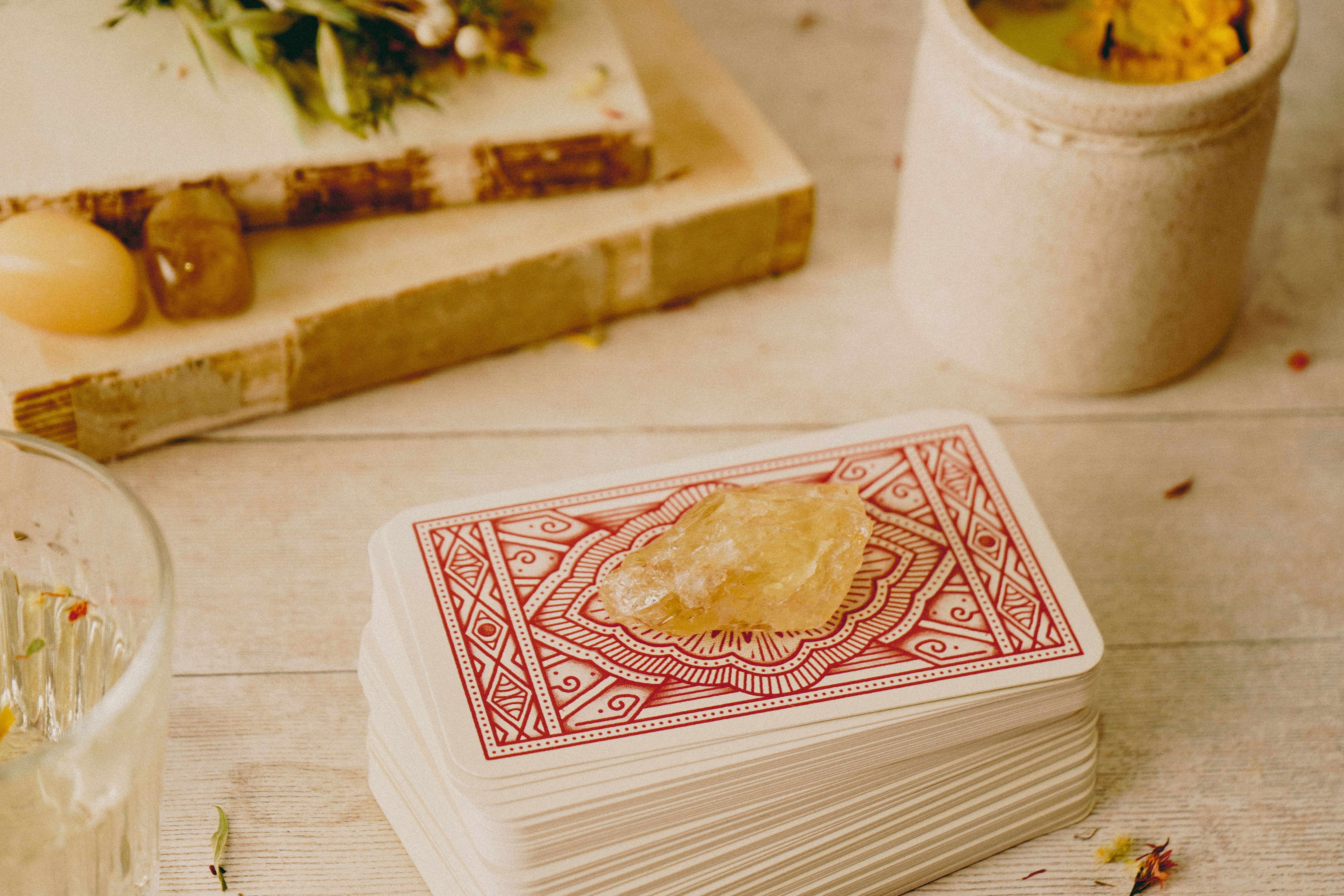 Tarot cards stacked with a citrine crystal, surrounded by spiritual items on a wooden table.