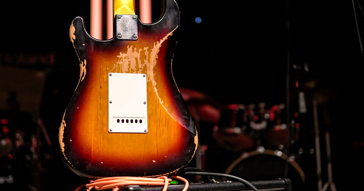 Close-up of a worn electric guitar with an amplifier on a dimly lit stage, creating a warm, vintage feel.