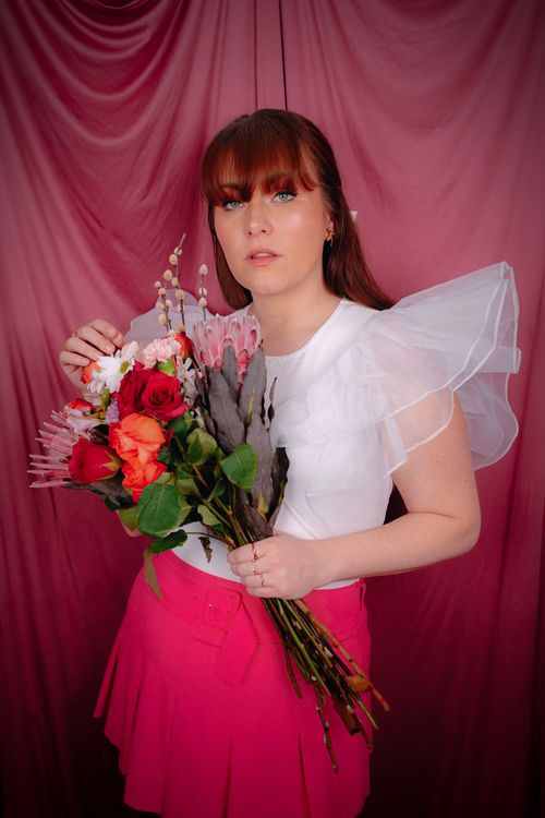 Free Woman in a white top and pink skirt holding a vibrant floral bouquet against a pink backdrop. Stock Photo
