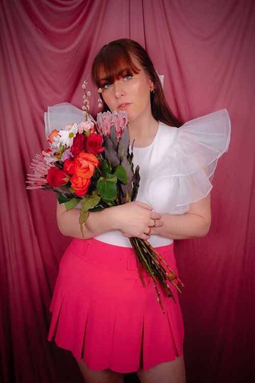 Free A woman in spring fashion holds a colorful bouquet against a pink backdrop. Stock Photo