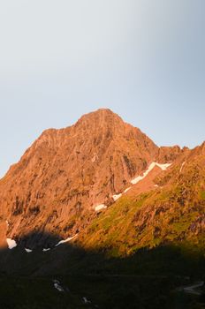 Sunlit mountain peak during golden hour with lingering snow patches.