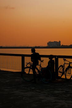 Capturing cyclists silhouetted against a vibrant sunset by the river.