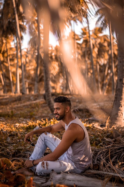 Man Sitting on Ground Surrounded by Palm Trees