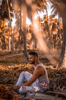 Young man sitting among palm trees in a bright tropical setting, showcasing casual fashion and a relaxed vibe.